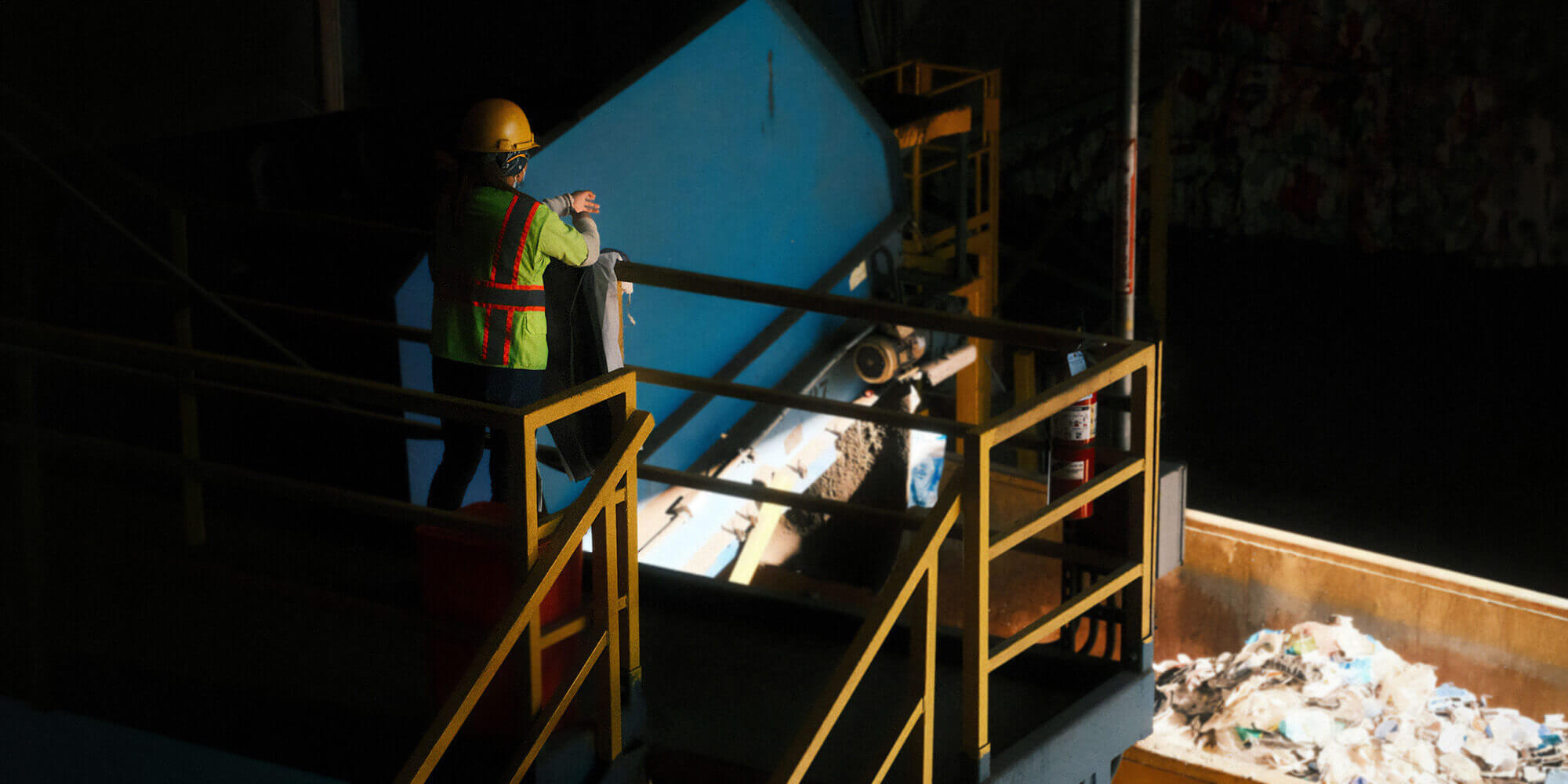 Worker in a safety vest and hard hat overlooking a recycling facility.