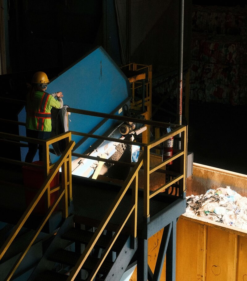 Worker in a safety vest and hard hat overlooking a recycling facility.