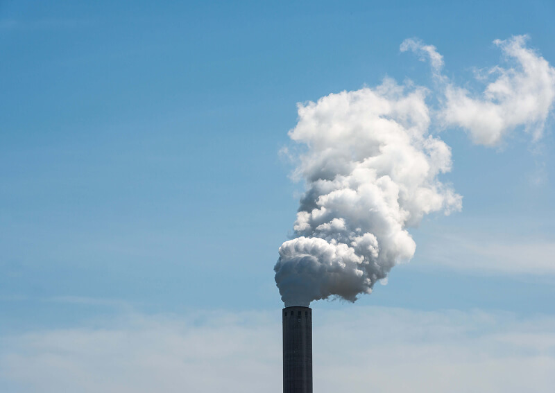 White smoke billowing from an industrial smokestack against a blue sky.