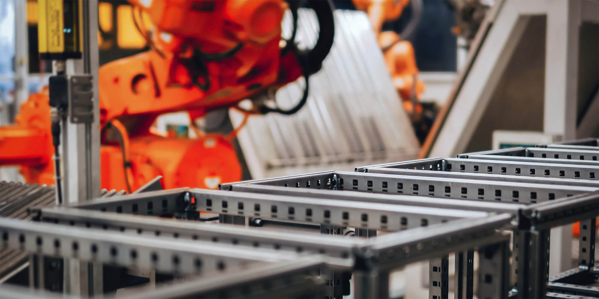 An orange robotic arm assembling metal frames on a factory production line.